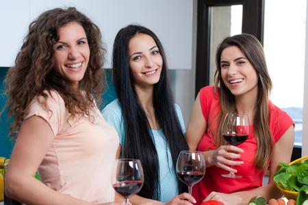 Happy female friends enjoying in the kitchen, spending great time, drinking wine and enjoying while cooking together.の写真素材