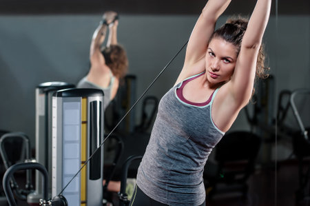 Young woman flexing muscles on cable gym machine exercising with hands