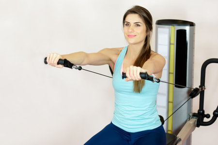 Young woman flexing muscles on cable gym machine exercising with hands - sport, fitness, lifestyle...