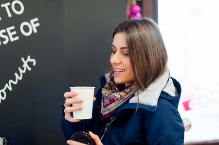 Young woman in a coffee shop holding a to go cup with coffee enjoying the flavor.の写真素材