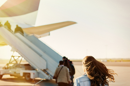 Woman tourist passager getting in to airplane at airport, walking from the terminal to the plane.の写真素材