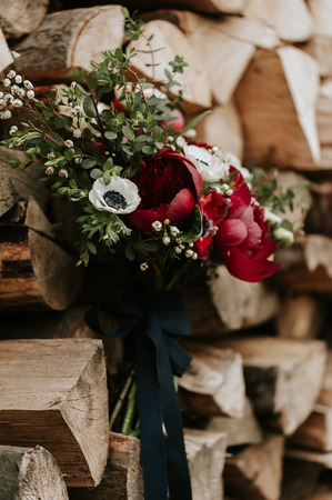 Beautiful bohemian wedding bouquet with red peonies and white anemones, over wood background.の写真素材