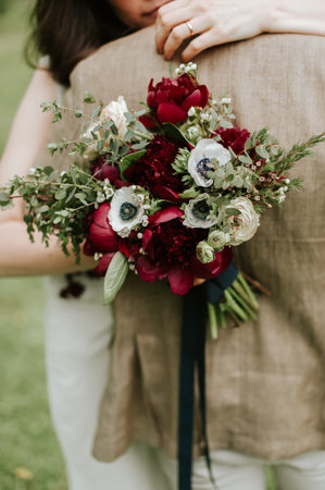 Couple hugging holding a bouquet of red peonies and white anemonesの写真素材