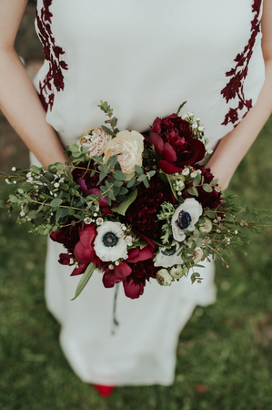 Bohemian bride holding her flower bouquet with red peonies and white anemones.の写真素材