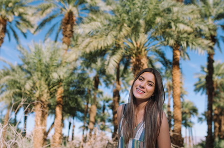 Holidays woman smiling at camera on tropical beach summer vacation with palm trees and date palmsの写真素材