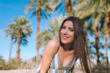 Holidays woman smiling at camera on tropical beach summer vacation with palm trees and date palmsの写真素材