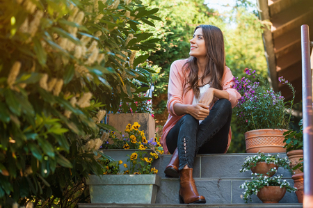 Relaxed young female smiling and looking side, sitting on home terrace. Hobby and resting leisure concept.の写真素材