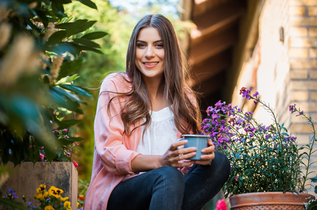 Relaxed young female smiling and looking at camera, sitting on home terrace, holding a mug drinking a hot beverage. Hobby and resting leisure concept.の写真素材