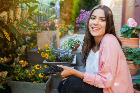 Pretty young girl smiling and gardening in pots on the terrace,at home, with working gloves. Gardening as hobby and leisure concept.の写真素材