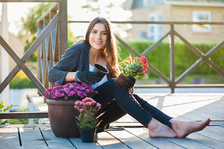 Pretty young girl smiling at camera and gardening in pots on the terrace,at home, with working gloves. Gardening as hobby and leisure concept.の写真素材