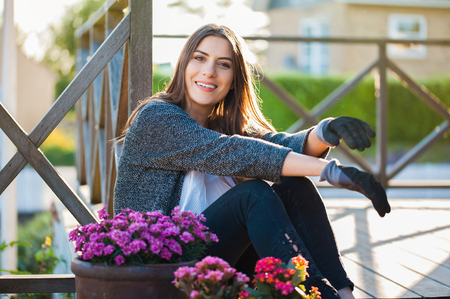 Beautiful young girl smiling and looking at camera, gardening in pots on the terrace,at home, with working gloves. Gardening as hobby and leisure concept.の写真素材