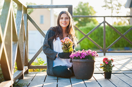 Smiling young female gardening in pots on the terrace,at home, with working gloves, looking at camera and smiling. Gardening as hobby and leisure concept.の写真素材
