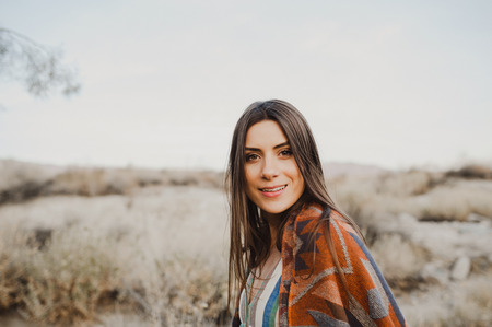 Boho woman with windy hair in the desert nature, turning her head and smiling at camera.  Artistic photo of young hipster traveler girl in gypsy look, in Coachella Valley in a desert valley in Southern California.の写真素材