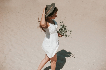 Beautiful young hipster girl enjoying a sunny beautiful day walking along the beach picking wild plants and looking happy.の写真素材