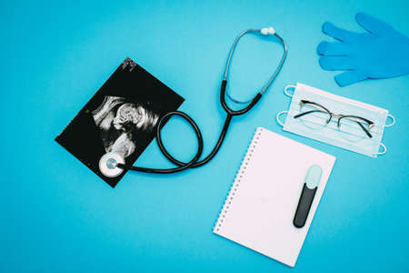 Stethoscope, notepad, marker, glasses, disposable gloves, medical mask and ultrasound picture of a child on a light blue background. Flat-lay, top view with place for your text. Medical trends and concept.の写真素材