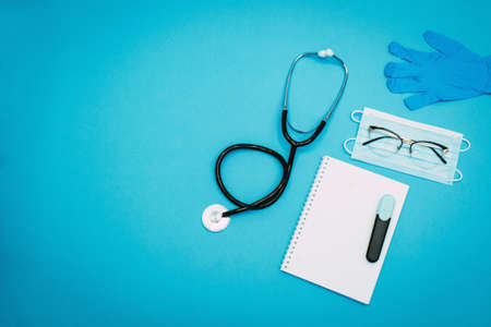 Stethoscope, notepad, marker, glasses, disposable gloves and a medical mask on a light blue background. Flat-lay, top view with place for your text. Medical trends and concept.の写真素材