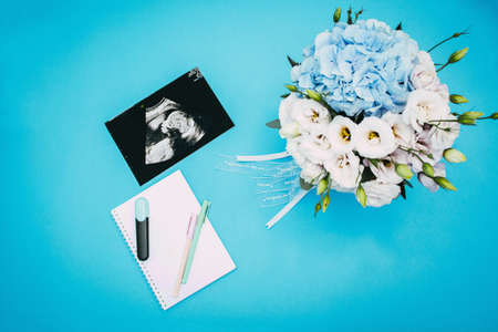 Marker, notepad, ultrasound picture of a child, bouquet of flowers and pregnant book on a light blue background. Flat-lay, top view with place for your text. Medical trends and concept.の写真素材