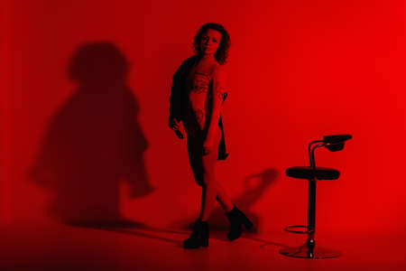 Fashion model in stylish clothes at the neon lights in the studio. Studio portrait of a sexy woman in a leather jacket, bodysuit and boots on a red ultraviolet background in a nightclubの写真素材