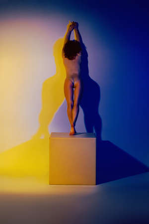Fashion model in stylish clothes at the neon lights in the studio. Studio portrait of a sexy woman in a bodysuit on a blue and yellow ultraviolet background in a nightclub.の写真素材