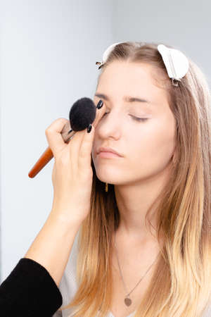 Professional makeup artist applies makeup to a beautiful girl model. The face of a beautiful girl with clean skin. Real life Makeup and Cosmetology conceptの写真素材