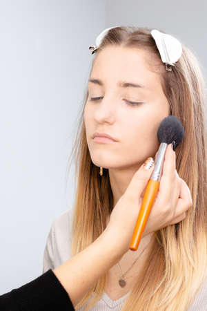 Professional makeup artist applies makeup to a beautiful girl model. The face of a beautiful girl with clean skin. Real life Makeup and Cosmetology conceptの写真素材