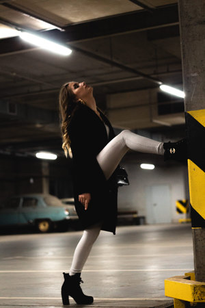 Attractive young brown-haired woman posing in an underground parking. Girl model in black coat...