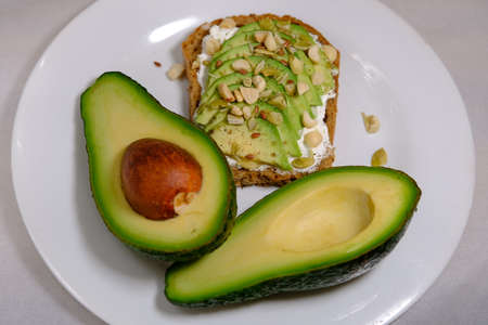 Avocado sandwiches, half of avocado, with peanuts and pumpkin seeds on a white background and divided avocado fruit on the plateの写真素材