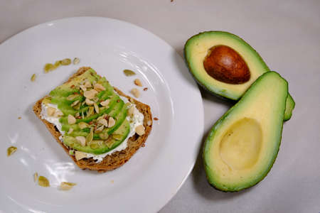 Avocado sandwiches, half of avocado, with peanuts and pumpkin seeds on a white background and divided avocado fruit near plateの写真素材