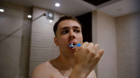 Young man brushing his teeth in bathroom. Beautiful interior.の写真素材