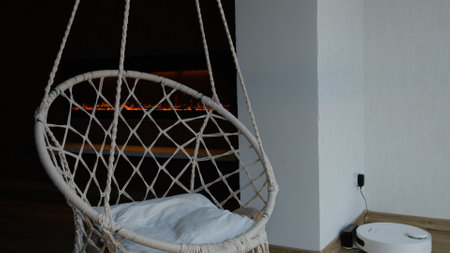 White wicker swing chair, cute interior. White bedroom, cozy house. The interior design of the nursery concept, big window vacuum robot and fireplace.の写真素材