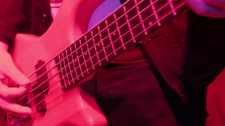 Hands of rock musician playing the electric bass guitar on repetitin in red light.の写真素材