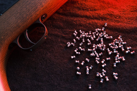 Rifle gun trigger with air pellets for hunting on cloth dark background with red light.