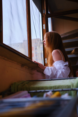 Young redhead Woman in white shirt Looks Out The Window on the balcony with the wash blured Deep In Thought red hairs ginger girl general planeの写真素材