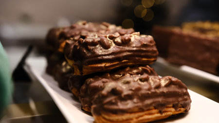 A delicious gourmet eclair filled with creamy custard, topped with crunchy peanuts, rich chocolate glaze, and a luxurious golden sprinkle, creating a visually appealing and indulgent dessert.の写真素材