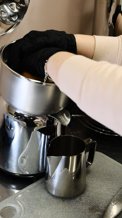 A barista in black disposable gloves squeezes fresh oranges on a professional juicer into a metal...