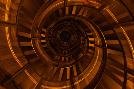 View from the bottom on the metal spiral staircase highlighted with orange neon