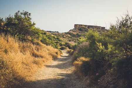 Dusty footpath under bright sun to the rock on the moountainの写真素材