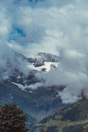 Snow covering the top of the mountain in Austrian Alps and green forest at the bottomの写真素材