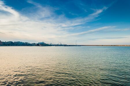 Warm evening in Italy on the sea shore with port on the backroundの写真素材
