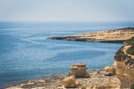 Blue water with wind stripes on it with yellow rocks and blue sky on the backgroundの写真素材