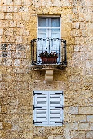 Small white window closed with shutters under the balcony with a closed door and a flower potの写真素材