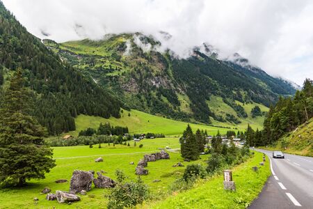 Road in the mountains covered with green forest under white cloudsの写真素材