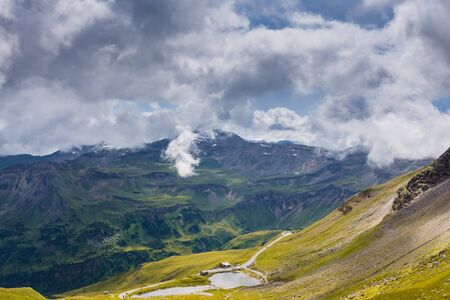 Austrian Alps under white cloudy sky and yellow sun rays in the morningの写真素材