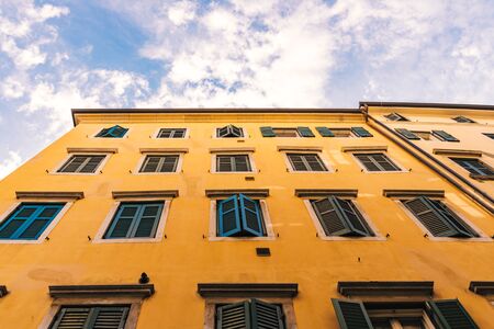 Closed green shutters of a yellow building and blue sky with small white clouds on the backgroundの写真素材