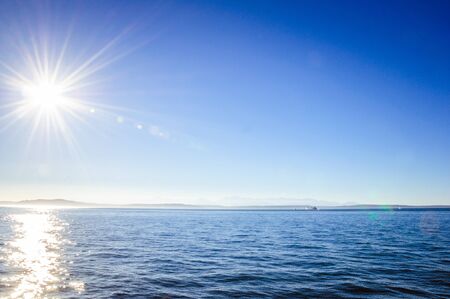 Bright sun during late afternoon over the calm ocean waterの写真素材