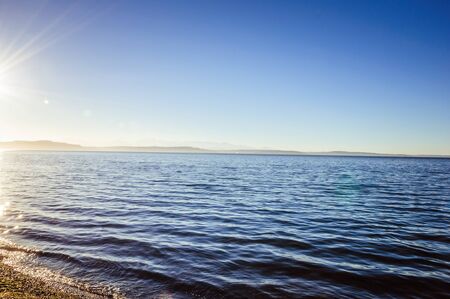 Bright sun during late afternoon over the calm ocean waterの写真素材
