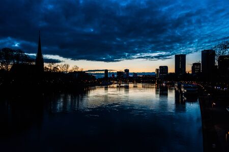 Evening sky over Frankfurt skyscrapers reflecting in the water of Mainの写真素材