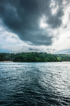 Small island, covered with forest and with dark clouds on the backgroundの写真素材