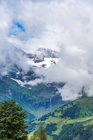 Austrian Alps covered with forest at the bottom and snow on the top with blue sky on the backgroundの写真素材