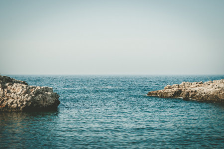 Calm sea with rocks on both sides, horizon and clear blue sky
